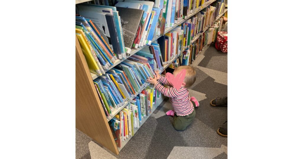 Child in front of three stacks of library books with pink heart in front of face.