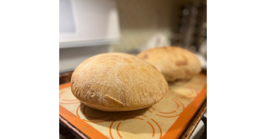 Two loaves of sourdough bread on a cream and orange silicone baking sheet