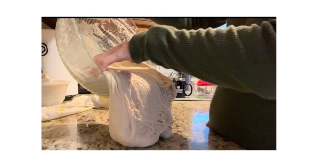 Hand pouring out dough onto a marble countertop. Girl wearing a green shirt.