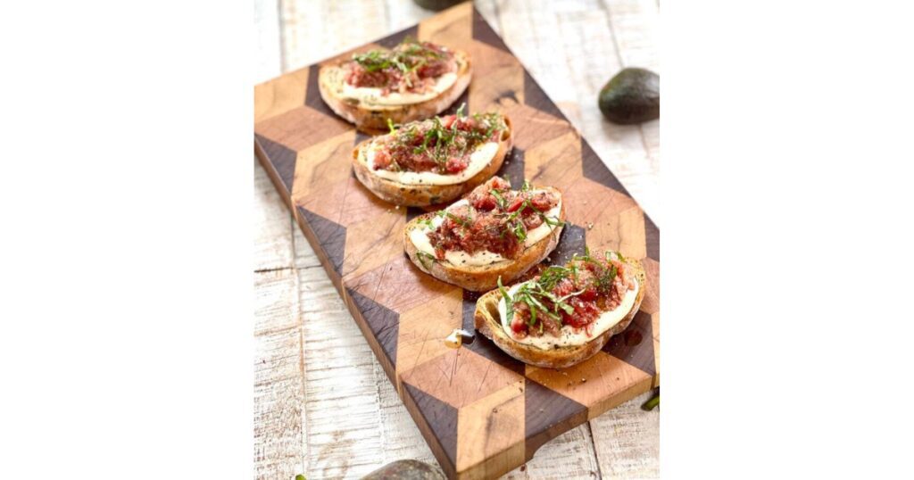 Four pieces of crostini with figs and spices on top. Crostini in a line on a wooden board.