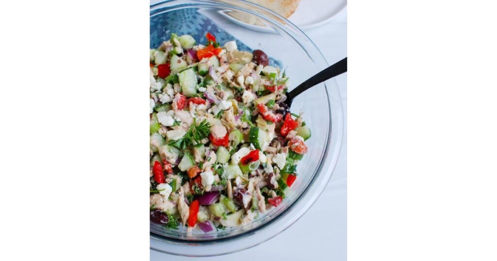 Colorful chopped salad with tuna, red pepper and cucumbers in a clear bowl with a spoon on the side.