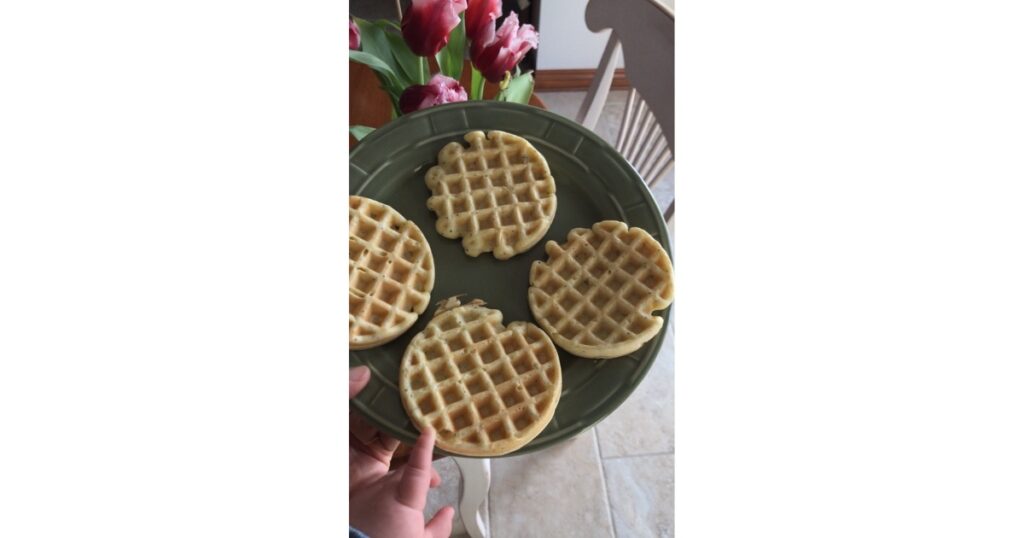 Four sourdough waffles on a green plate with tulips in the background.