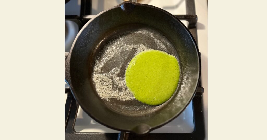 Green pancake on a cast iron skillet with butter