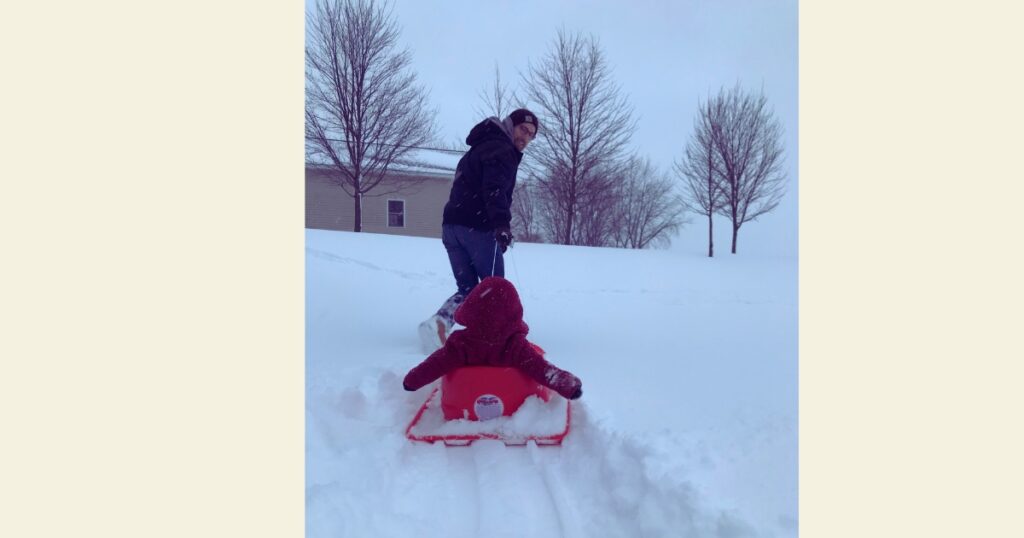 Dad pulling toddler in red sled through snow