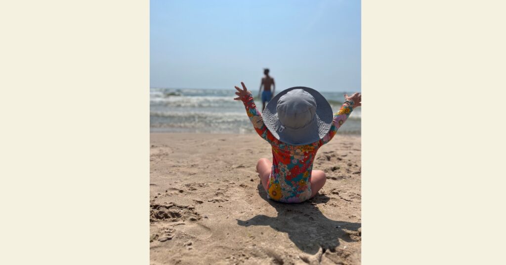 Child at beach in floral swim suit with arms in the air