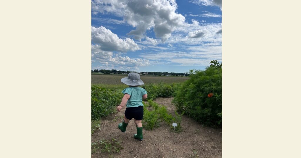 Toddler in garden with green rain boots and a cloudy sky