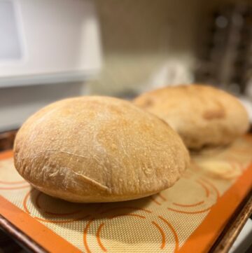 Two loaves of sourdough bread on a cream and orange silicone baking sheet