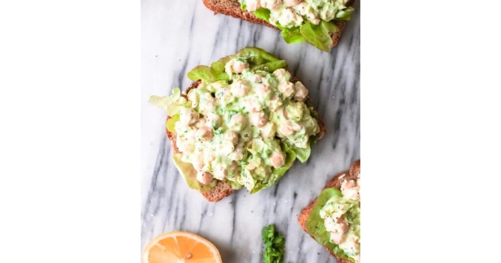 Chickpea salad on three slices of bread with lemon in left corner.