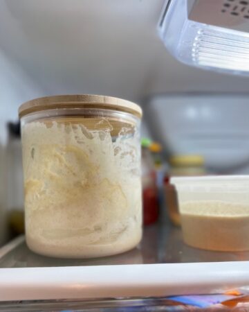 Sourdough in tall clear jar with a small container on right hand side in refrigerator
