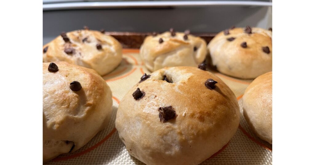 Five chocolate chip bagels bagels on a baking sheet.