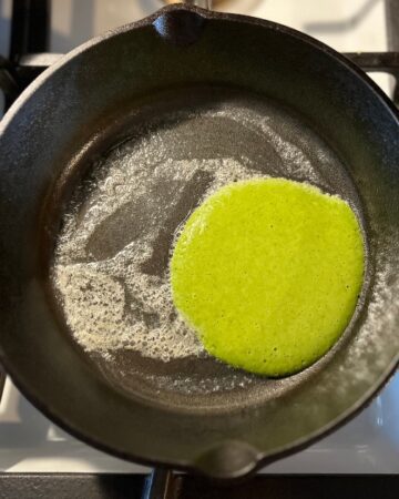 Green pancake on a cast iron skillet with butter