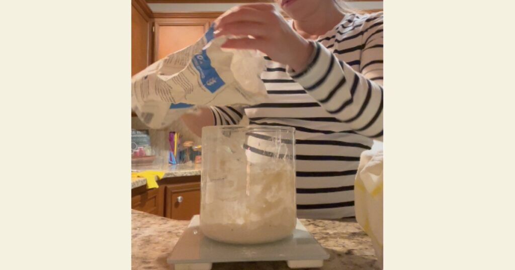 Girl in black and white shirt pouring flour into a container on a kitchen scale.
