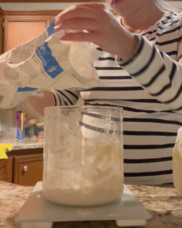 Girl in black and white shirt pouring flour into a container on a kitchen scale.