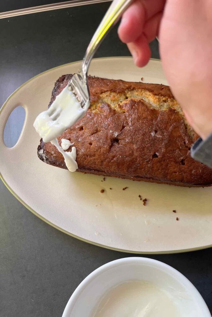 fork dripping glaze onto lemon bread on a plate.