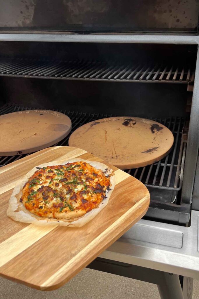 pizza on pizza peel placed onto a pizza pan on a traeger.
