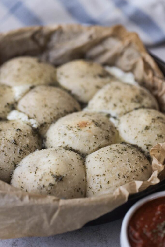 sourdough cheesy garlic rolls in a cast iron skillet with dried herbs on top.