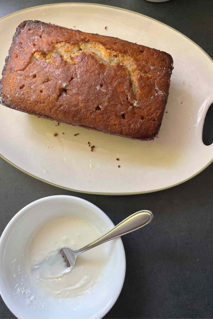 lemon poppyseed bread with lemon glaze in white bowl and fork in glaze bowl.