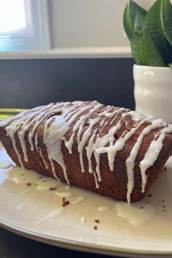 sourdough lemon yogurt loaf with glaze and green plant in background.