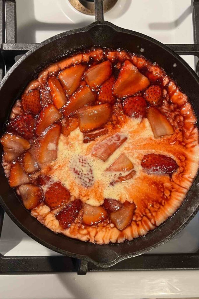 strawberry swirls on sourdough dutch baby batter in cast iron skillet.