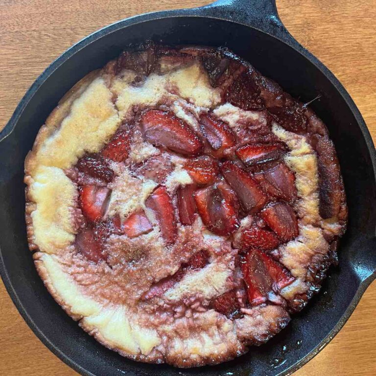 sourdough dutch baby with strawberries in cast iron skillet