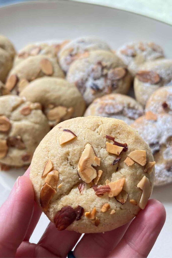 sourdoguh almond croissant cookie in focus with more cookies on platter behind it.