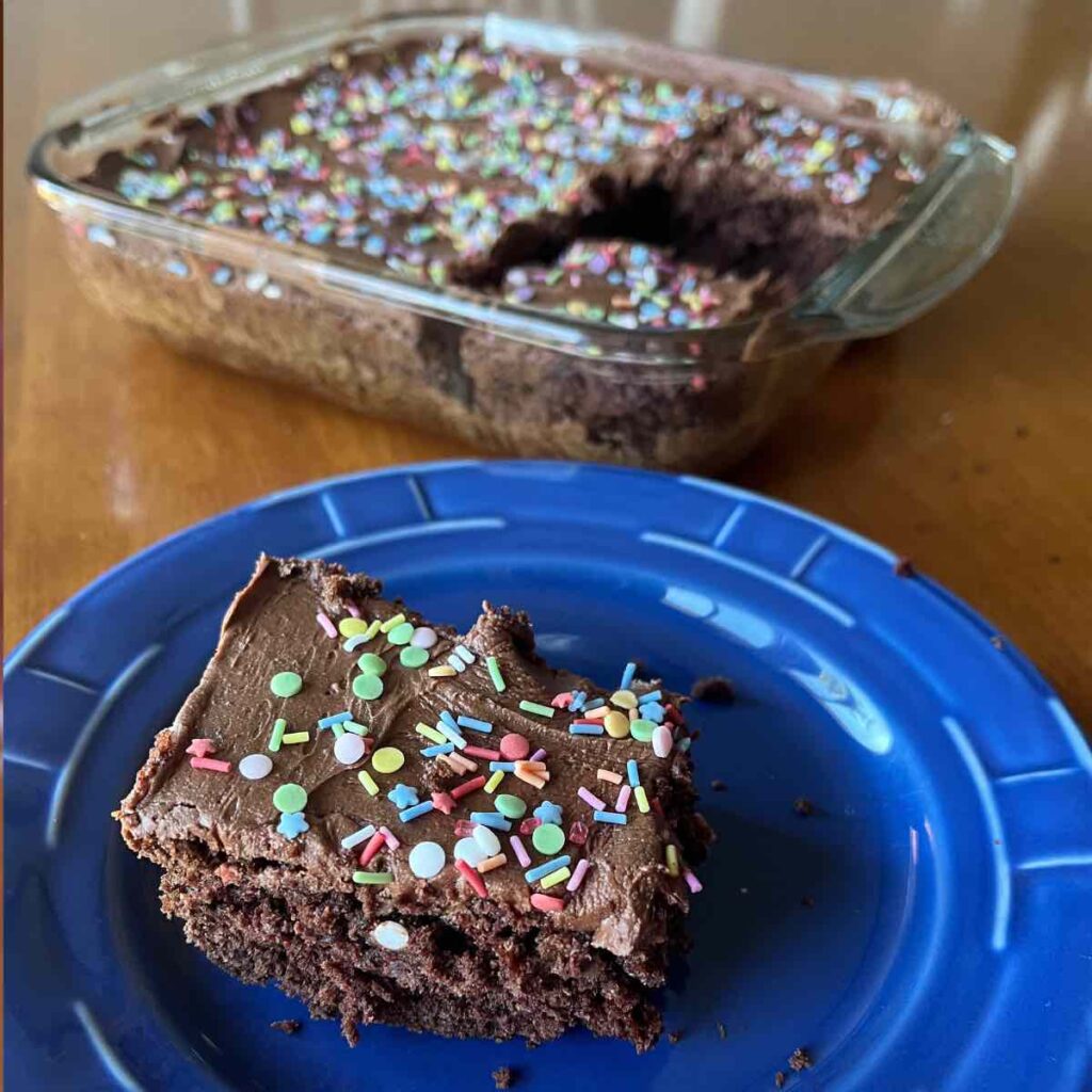 slice of sourdough brownie with frosting and sprinkles on a blue plate.