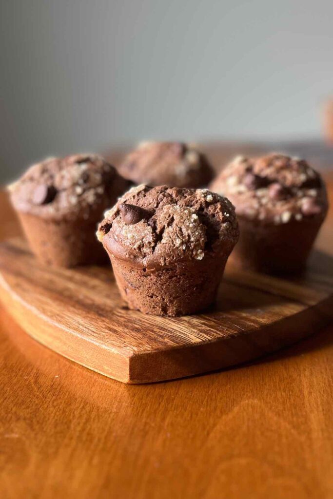 four double chocolate muffins on a wooden cutting board.