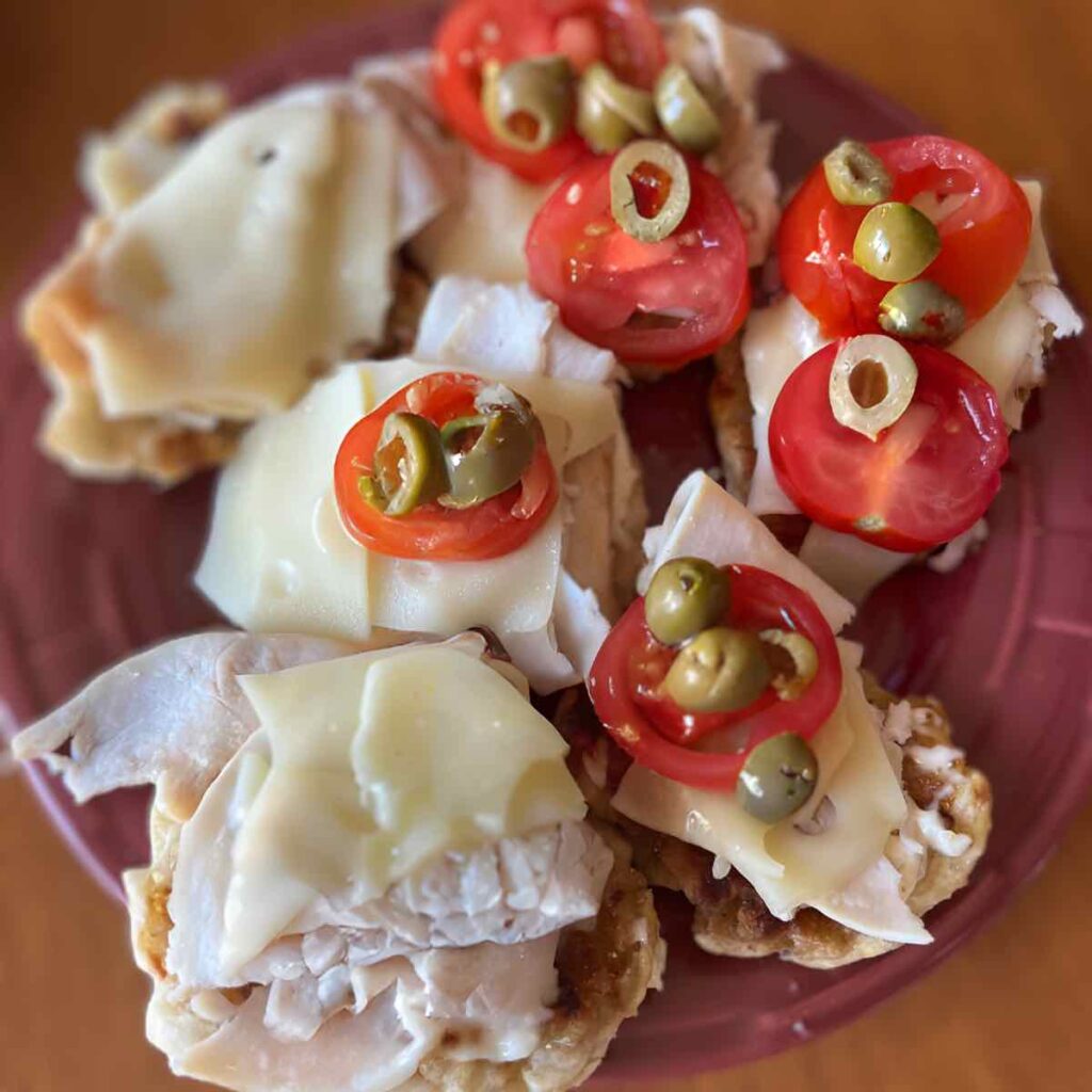sandwiches with lunch meat, cheese, tomato and green olives on a red plate.
