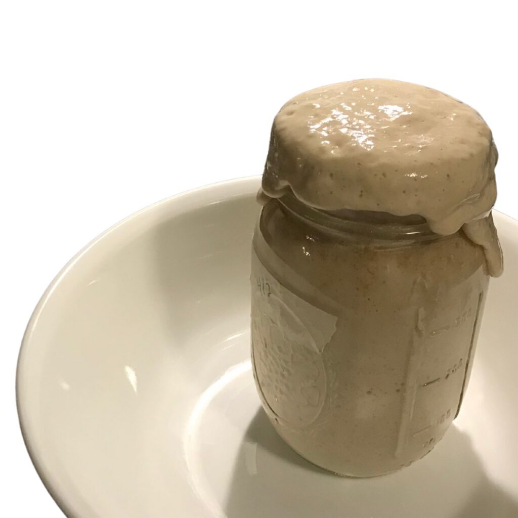 sourdough discard flowing over top of mason jar.