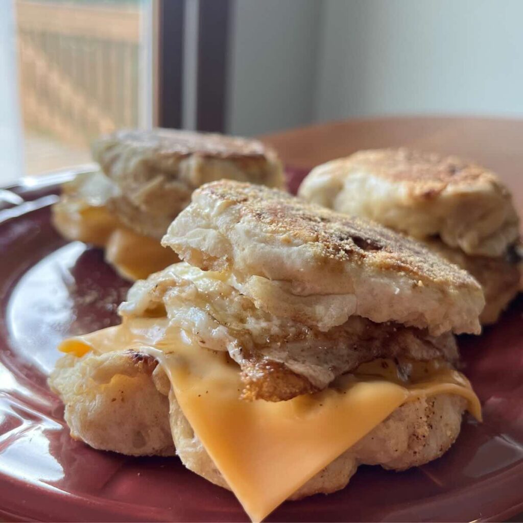 three sourdough English muffin breakfast sandwiches on a red plate.