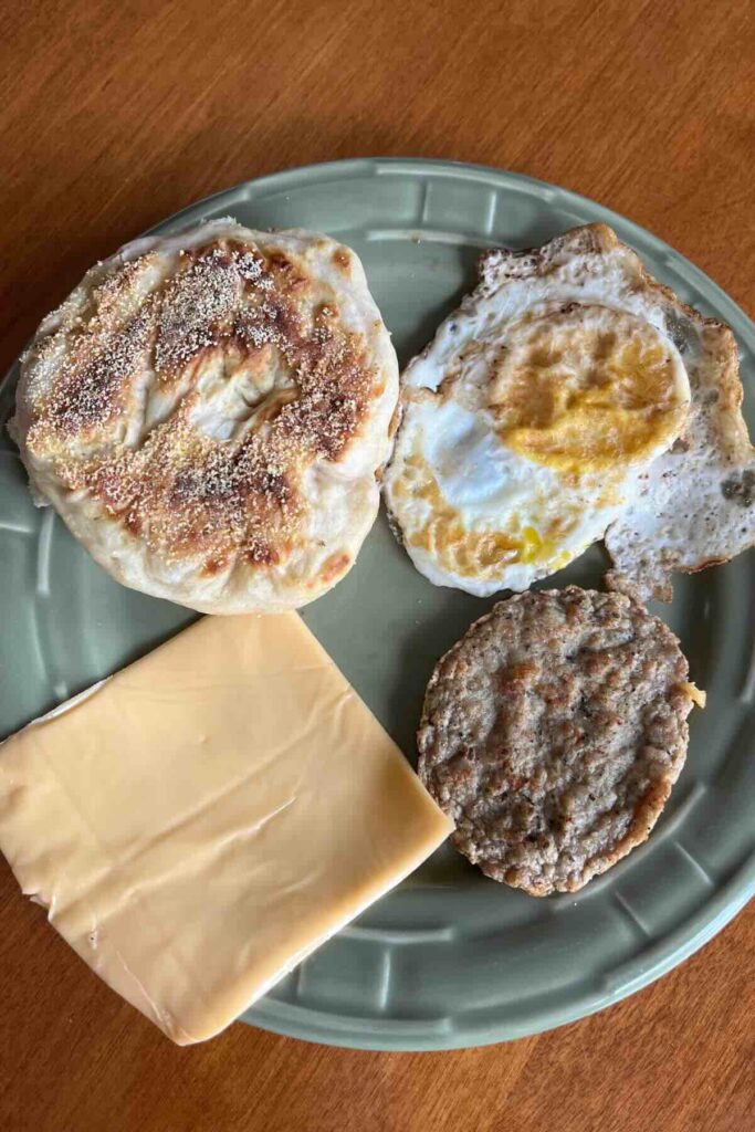 sourdough English muffin, fried egg, American cheese slice and breakfast sausage on a green plate.