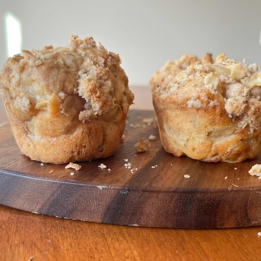 two apple crumble muffins on a wood cutting board.