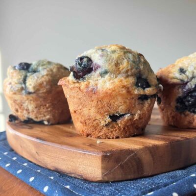 three sourdough blueberry muffins on a wooden cutting board.