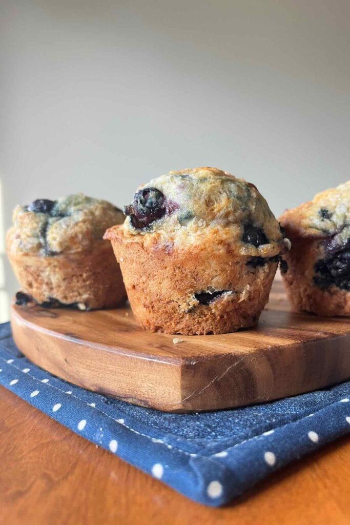 three sourdough blueberry muffins on a wooden cutting board.