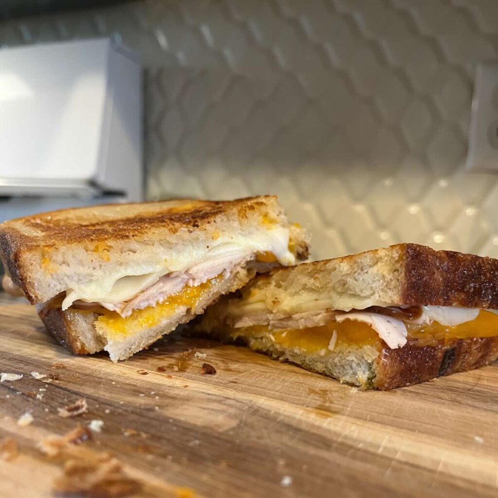 two slices of a grilled cheese sandwich on a wooden cutting board.