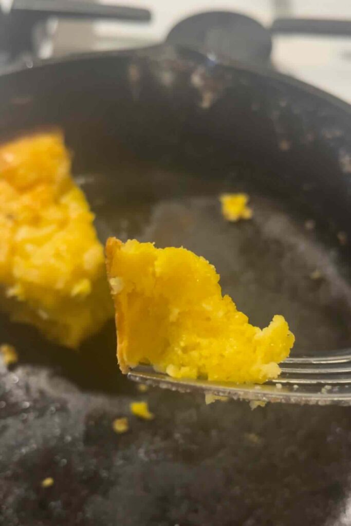 bite of savory dutch baby on a fork in front of a cast iron skillet.