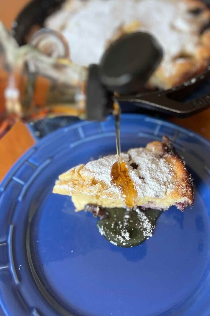 sourdough dutch baby with maple syrup and powdered sugar on a blue plate.