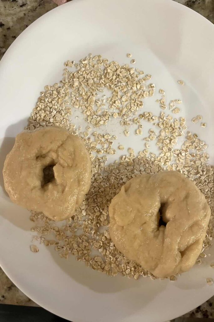 Roll honey oat bagels in oats on a plate.
